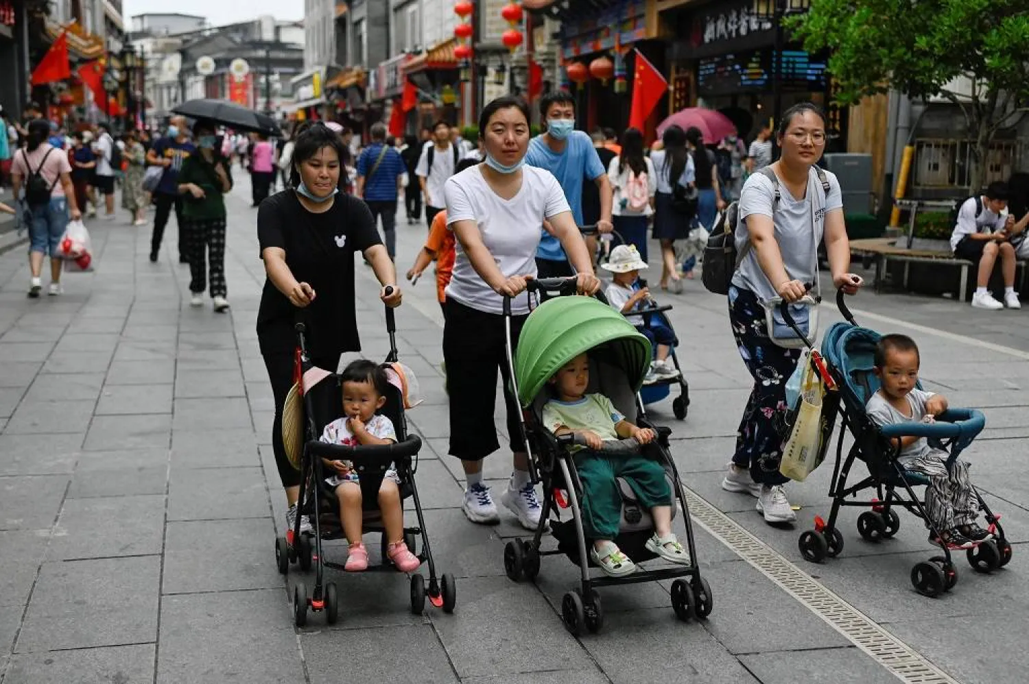 People push baby strollers along a business street in Beijing on July 13, 2021. (AFP)