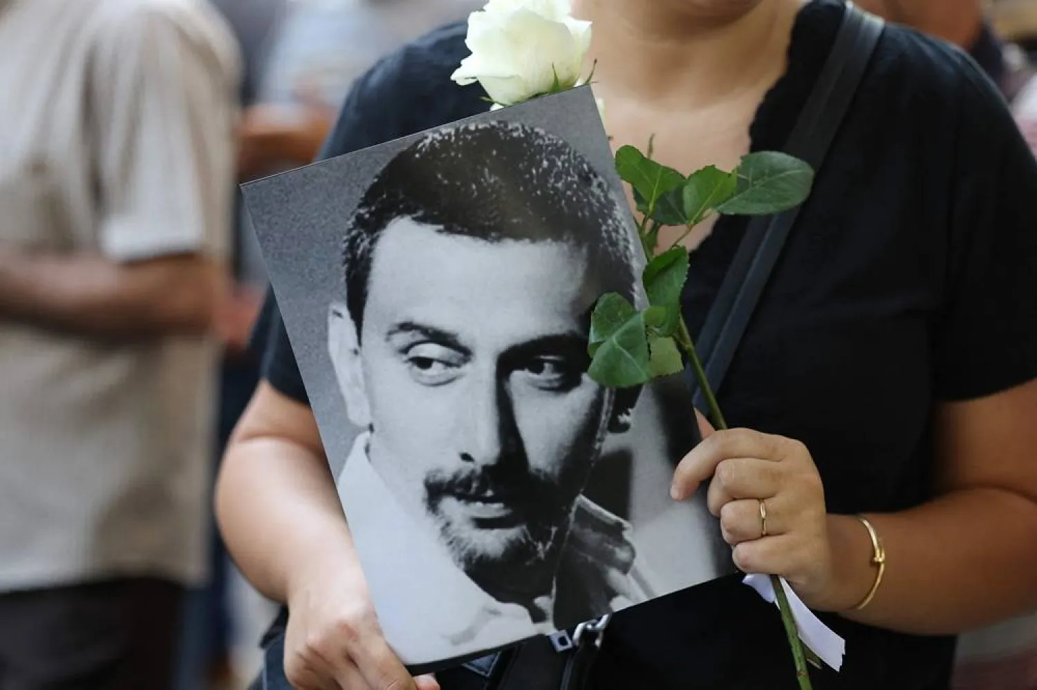 A mourner holds up a rose and a portrait of renowned Lebanese musician and composer Ziad Rahbani as crowds gathered outside Khoury Hospital in Beirut's central Hamra district to bid him farewell before his funeral procession on July 28, 2025. (AFP) 