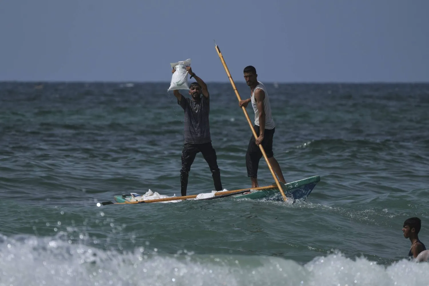 فلسطيني يحمل كيساً من دقيق المساعدات برفقة آخر يجذف قارباً صغيراً قبالة الزوايدة وسط قطاع غزة أمس (أ.ب)