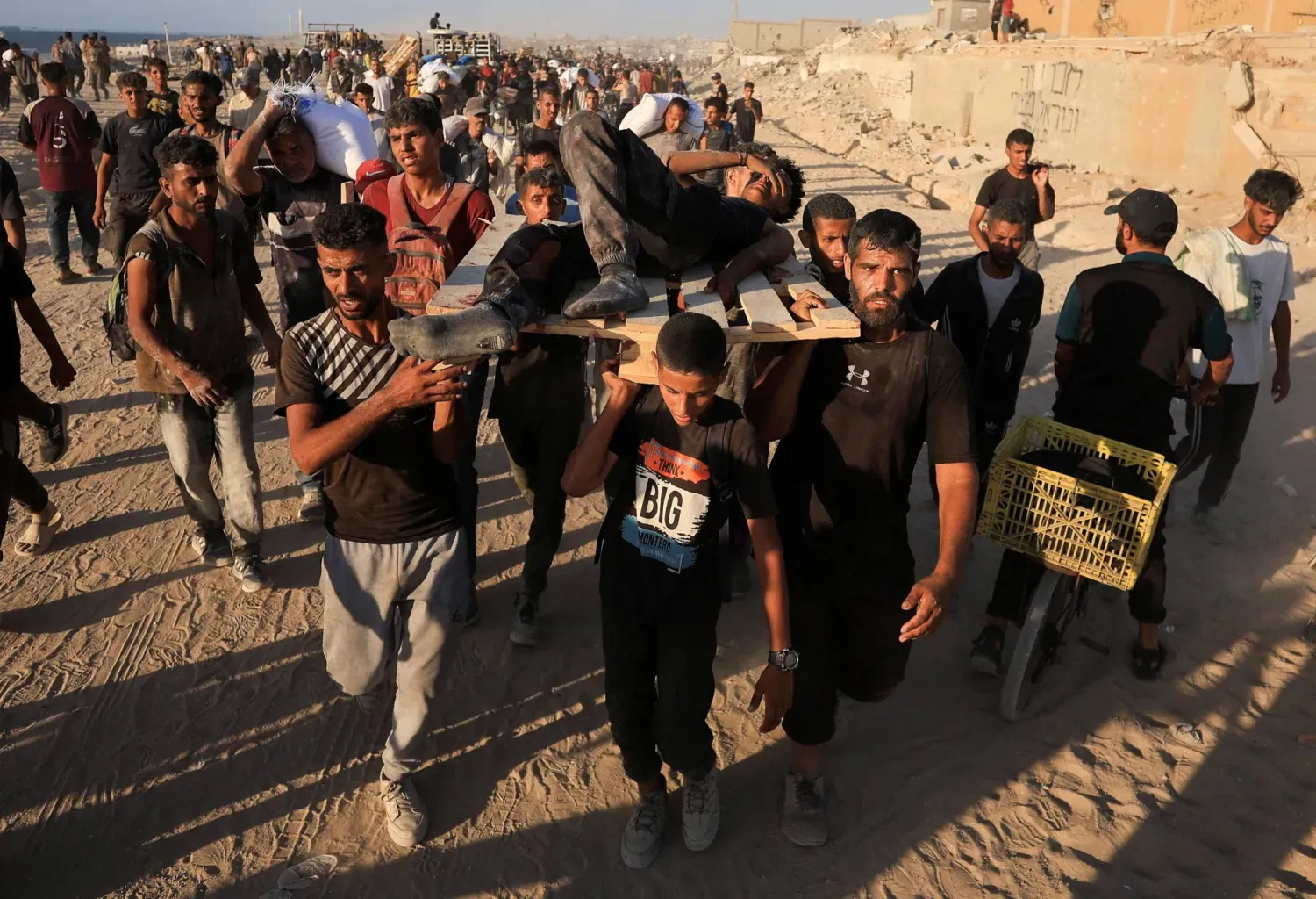 Filistinlilerden bazıları İsrail’in açtığı ateş sonucu yaralanan bir kişiyi taşırken, diğerleri ise İsrail üzerinden Gazze'ye giren yardım malzemelerini taşıyor (Reuters)