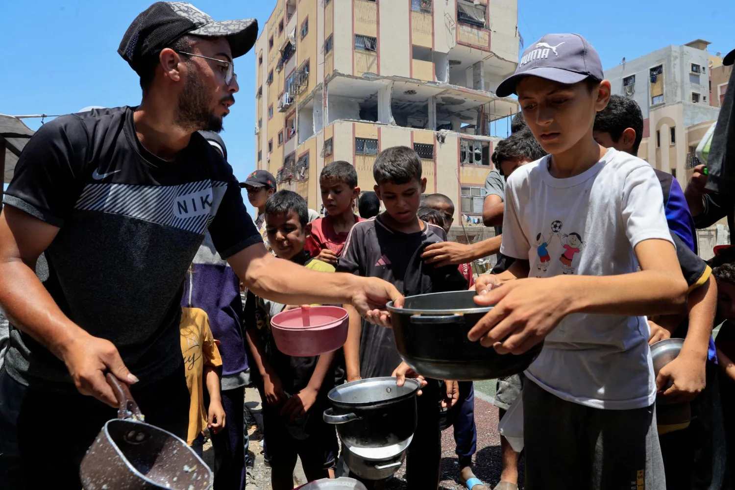 فلسطينيون يتجمعون لتلقي الطعام من مطبخ خيري وسط أزمة جوع في النصيرات بقطاع غزة (رويترز)