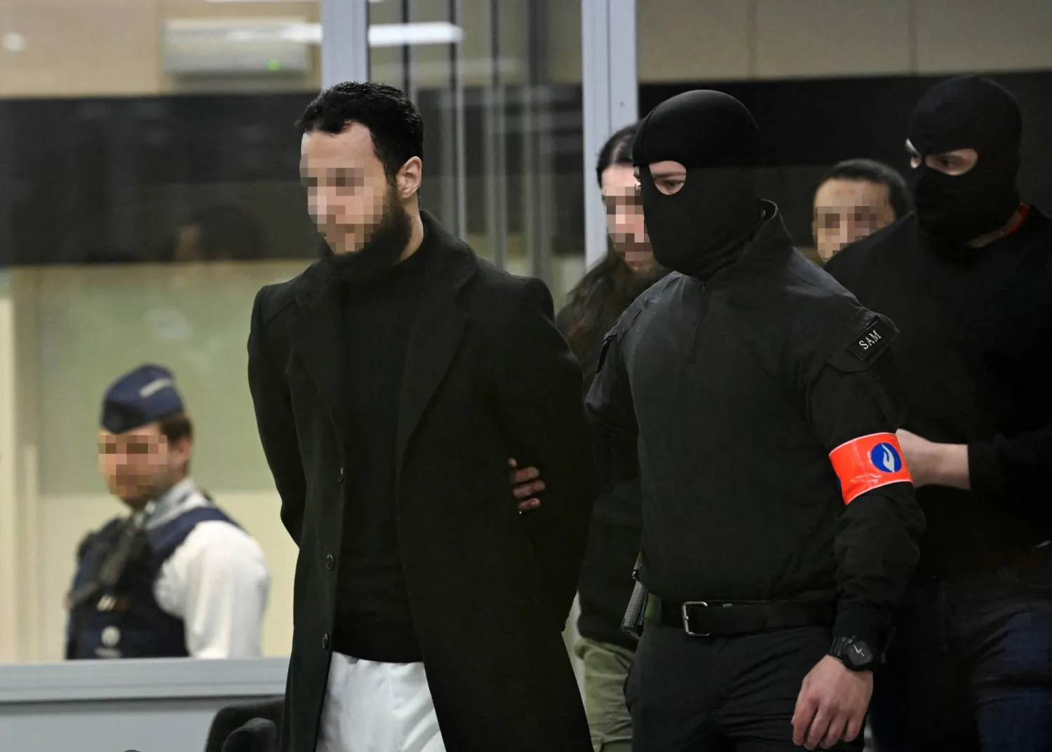 المتهمون صلاح عبد السلام وأسامة كريم ومحمد عبريني برفقة الشرطة لدى وصولهم إلى المحكمة خلال محاكمة منفذي هجمات بروكسل عام 2016 (رويترز)