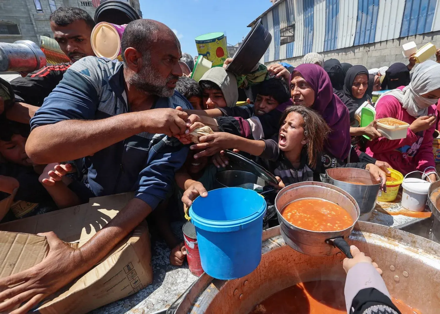 Gazze Şeridi'nin orta kesimindeki Nuseyrat Mülteci Kampı’nda bir aşevi tarafından dağıtılan yemekleri almak için bekleyen yerlerinden edilmiş Filistinliler (AFP)
