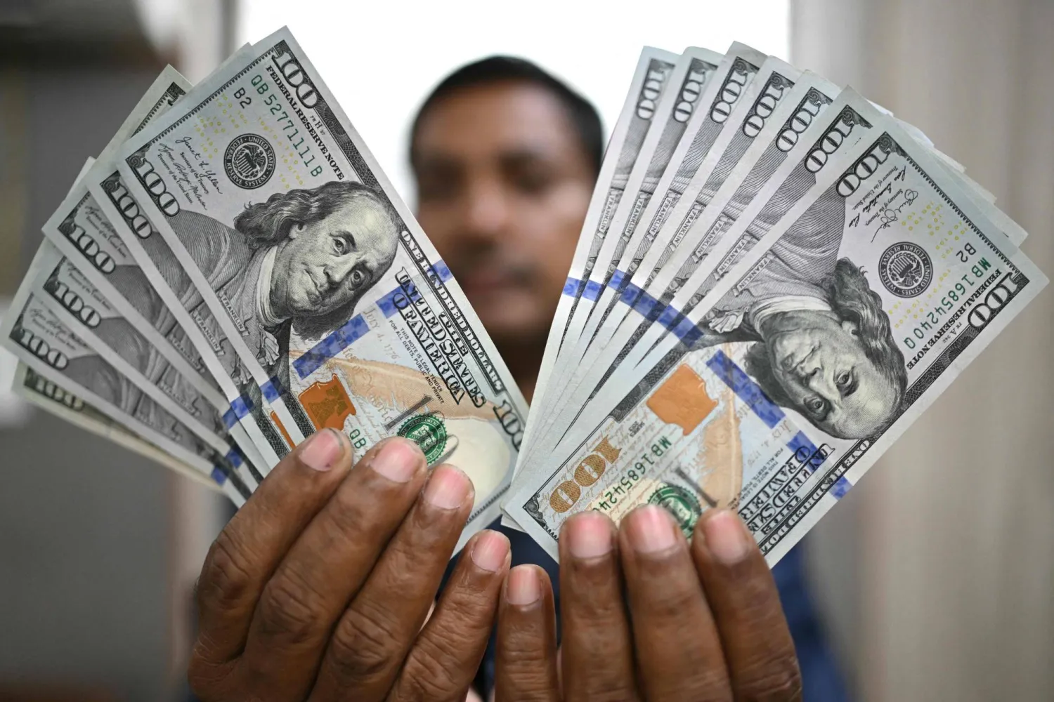 رجل يمسك أوراقاً نقدية من فئة 100 دولار في محل صرافة بالعاصمة الهندية نيودلهي (أ.ف.ب)