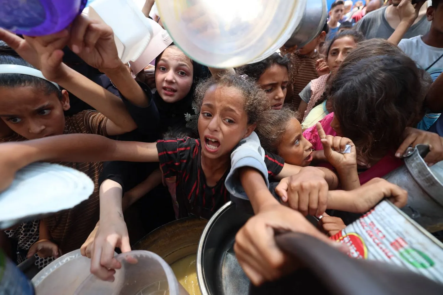 أطفال فلسطينيون يصطفون لتلقي وجبة ساخنة في نقطة توزيع طعام بالنصيرات (أ.ف.ب)