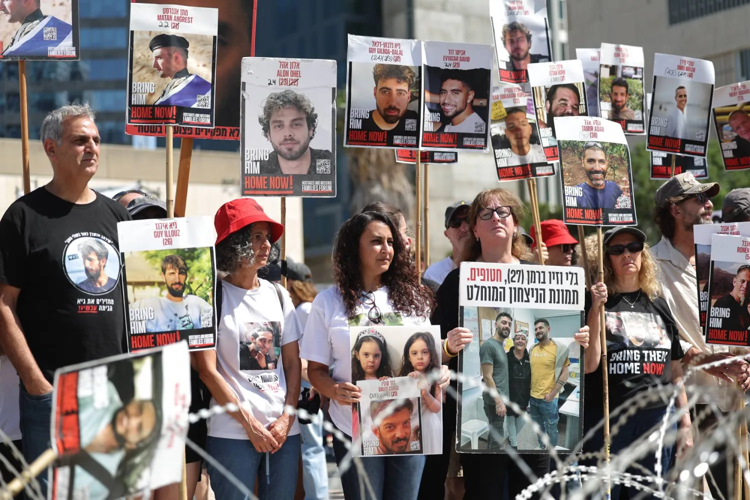 عائلات وأنصار الرهائن الإسرائيليين في غزة يحملون صوراً لهم قرب سياج من الأسلاك الشائكة خلال مظاهرة تدعو إلى وقف إطلاق النار واتفاق لإطلاق سراحهم (إ.ب.أ)