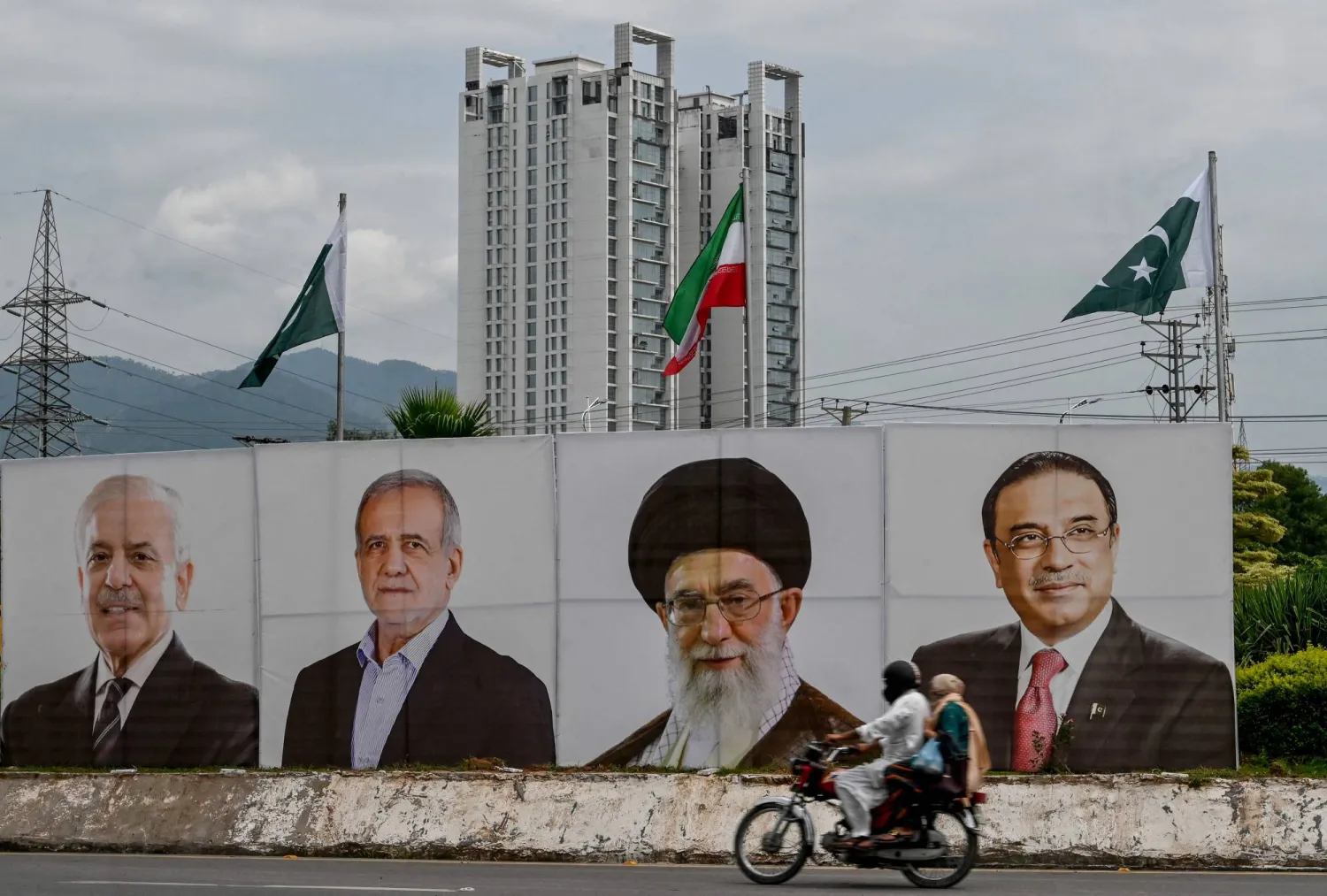 سائق دراجة يمر بجانب لافتة عليها صور (من اليسار إلى اليمين) رئيس الوزراء الباكستاني شهباز شريف والرئيس الإيراني مسعود بزشكيان والمرشد الإيراني علي خامنئي والرئيس الباكستاني آصف علي زرداري في إسلام آباد يوم 2 أغسطس 2025 (أ.ف.ب)
