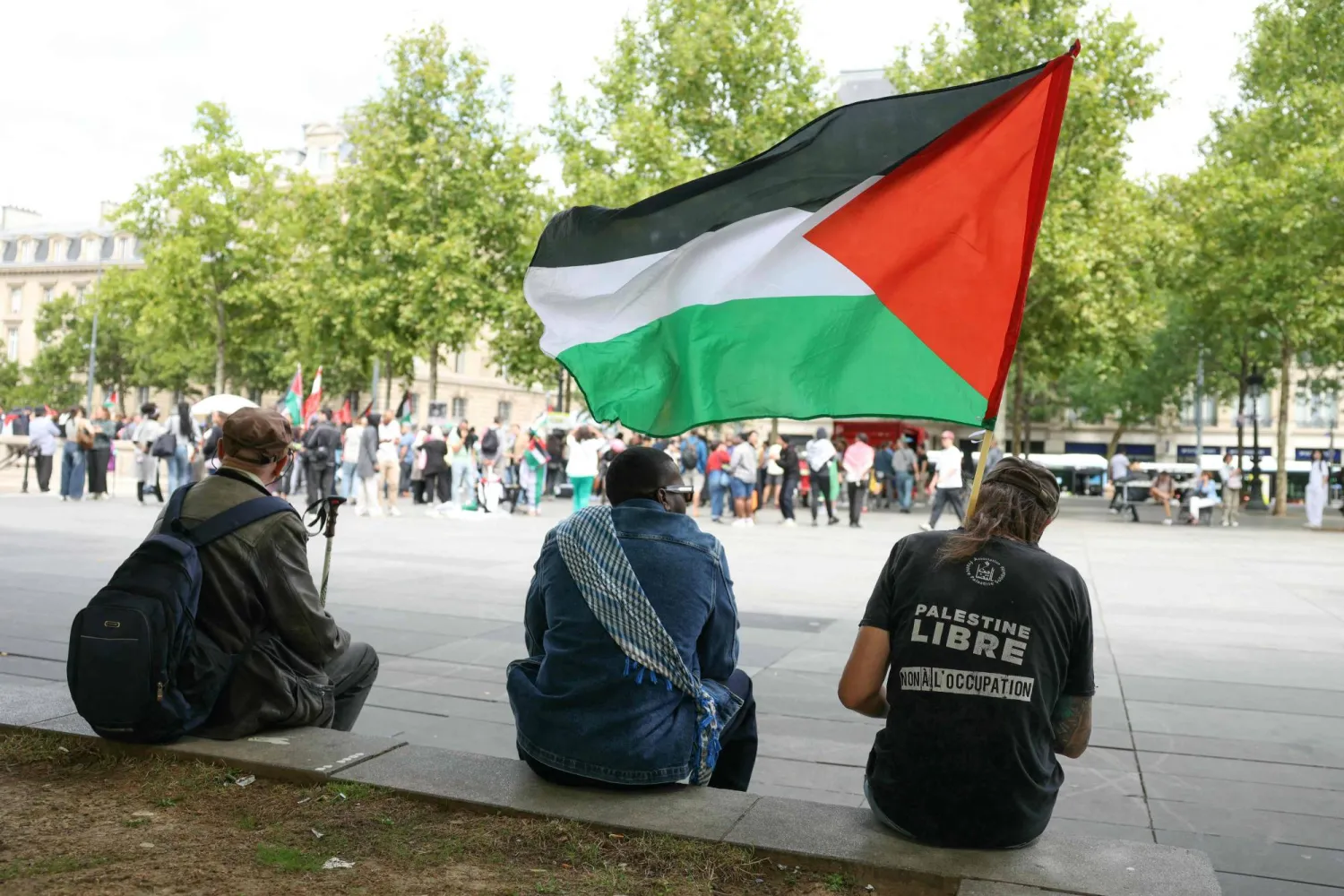 Protesters rest sitting on a wall holding a Palestinian national flag during a pro-Palestinian gathering against Israel's actions and the ongoing food shortages in the Gaza Strip with some released activist members of the Freedom Flotilla vessel Handala, at Place de la Republique, in Paris, on August 2, 2025. (Photo by Thomas SAMSON / AFP)
