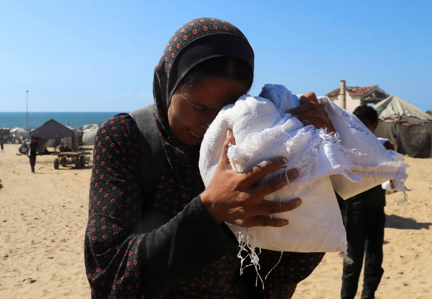 فلسطينية تحتضن جوالاً صغيراً من الطحين خارج خيمتها في مدينة غزة (رويترز)