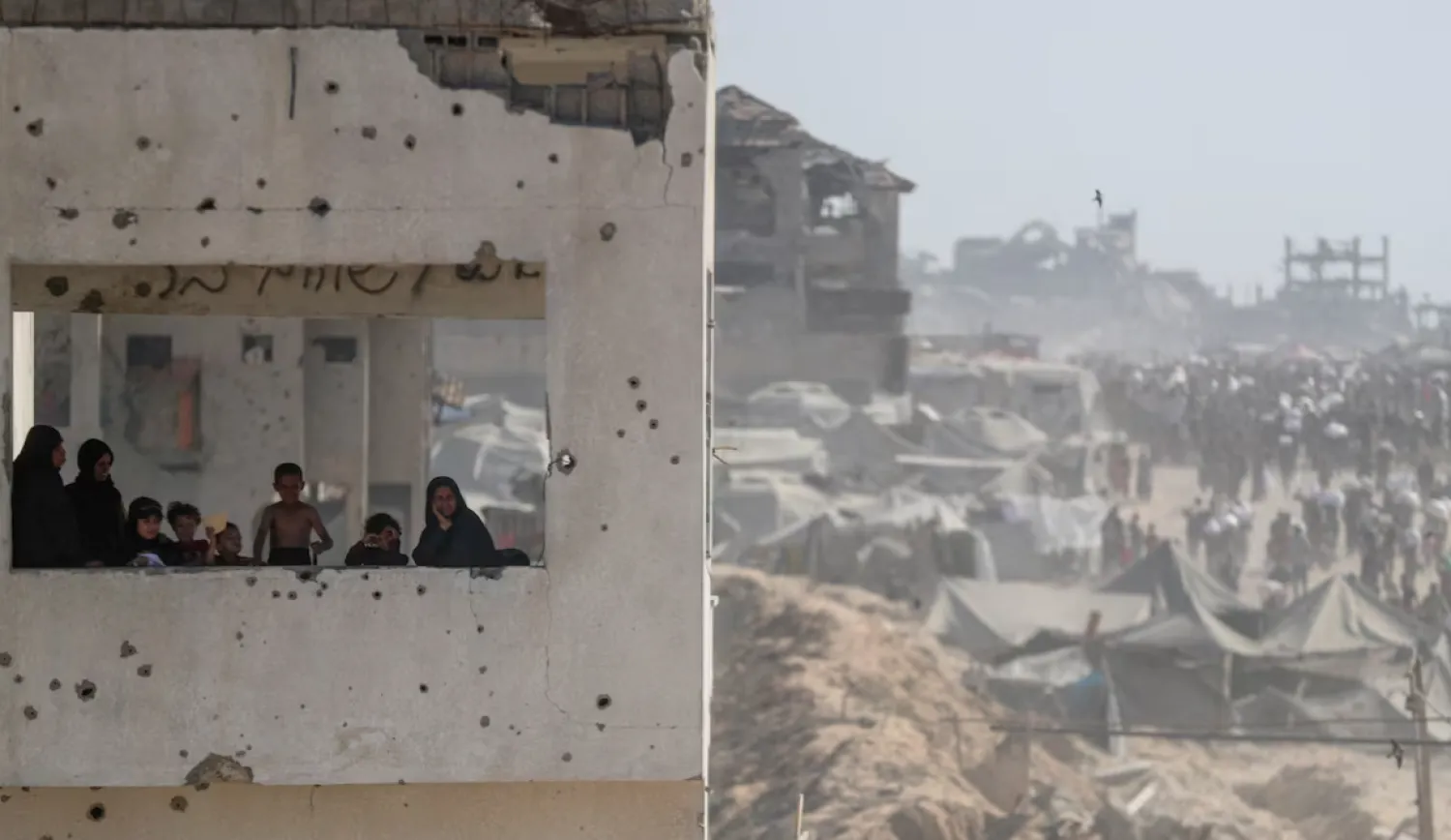 Women and children look out from a damaged building as Palestinians carry aid supplies that entered Gaza through Israel, in Beit Lahia, northern Gaza Strip, August 2, 2025. REUTERS/Mahmoud Issa