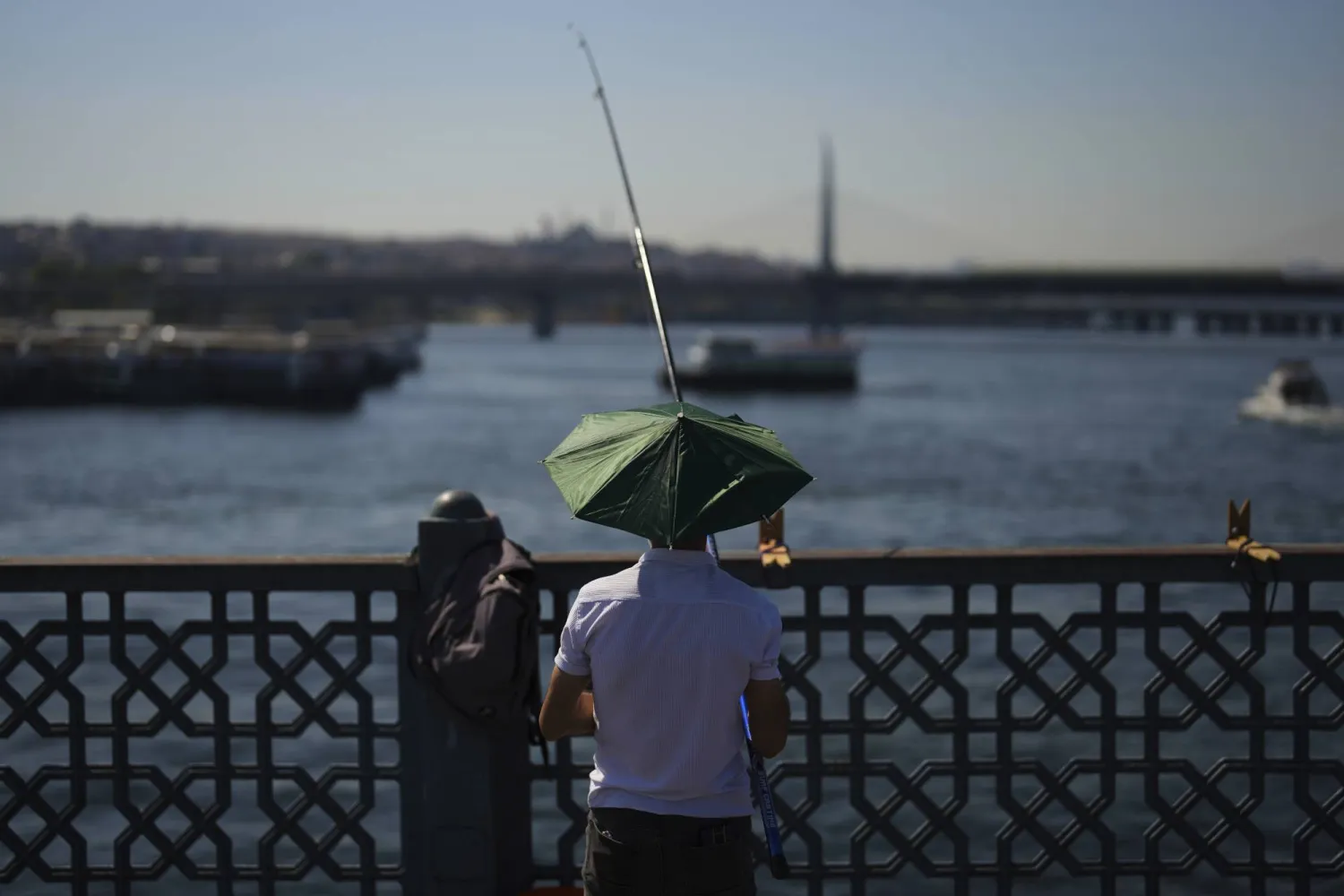 رجل يلقي بسنارة صيد بمضيق البوسفور عند جسر غلطة خلال يوم صيفي حار في إسطنبول (أ.ب)