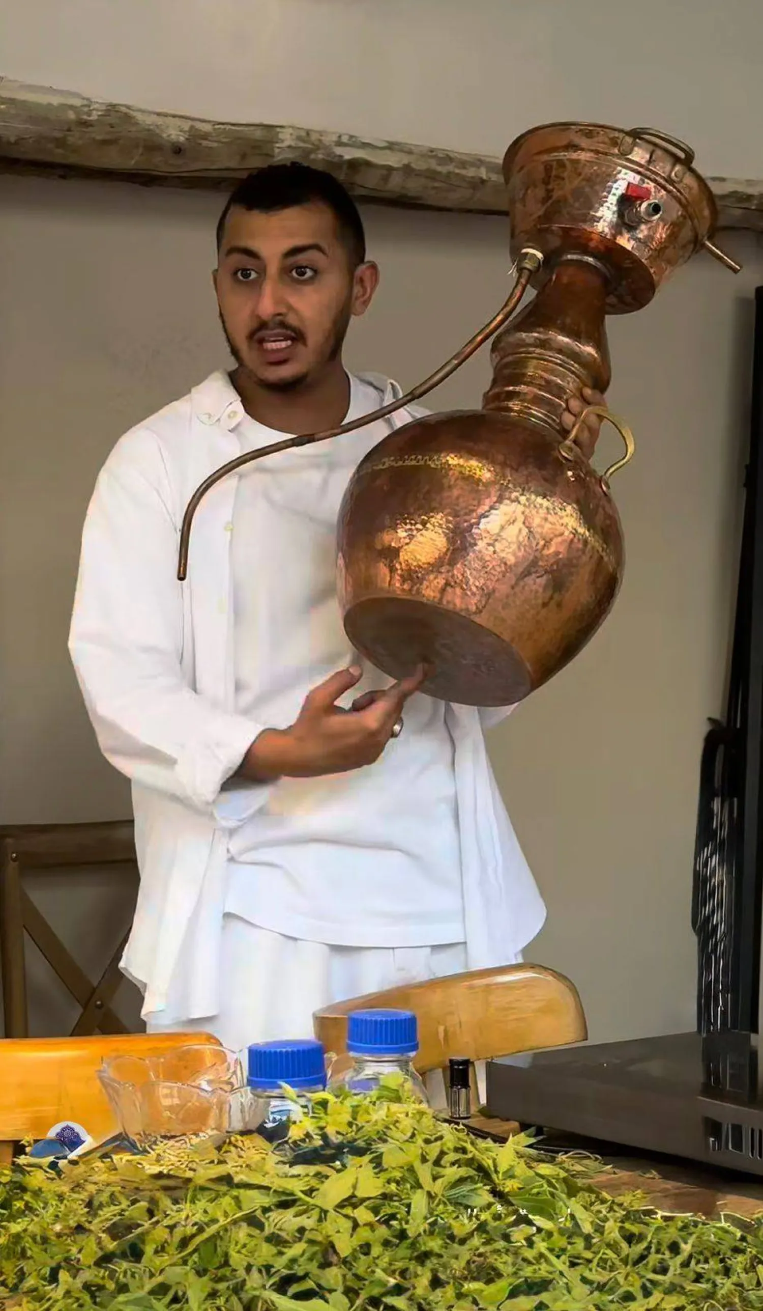عزام آل حمدان يشرح عملياً تقطير الزهور في إحدى ورش العمل التي يقدمها في معمله بجدة التاريخية (الشرق الأوسط)