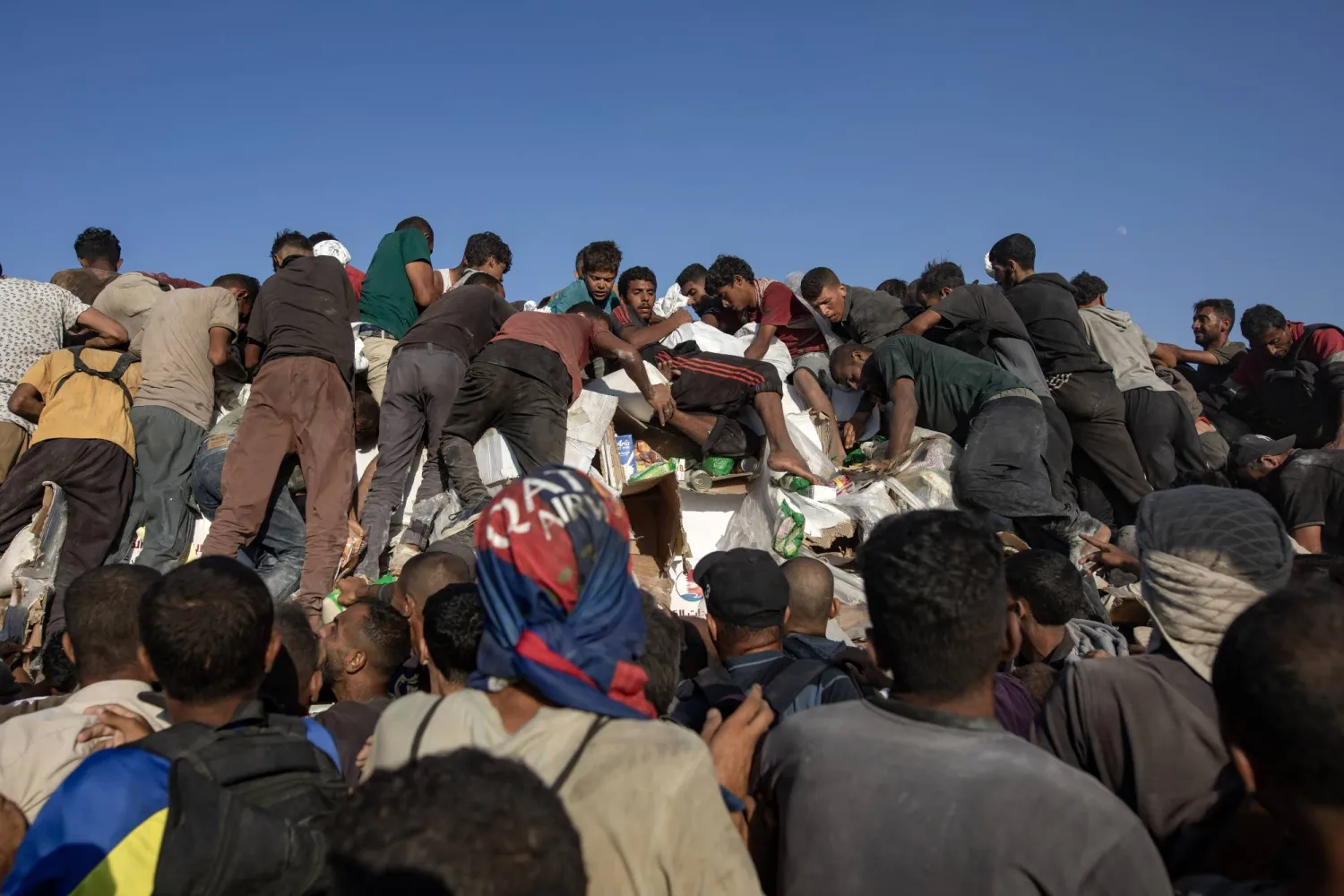 فلسطينيون يتسلقون شاحنات مساعدات للحصول على الطعام بالقرب من نقطة توزيع الغذاء في ممر موراج جنوب خان يونس (إ.ب.أ)