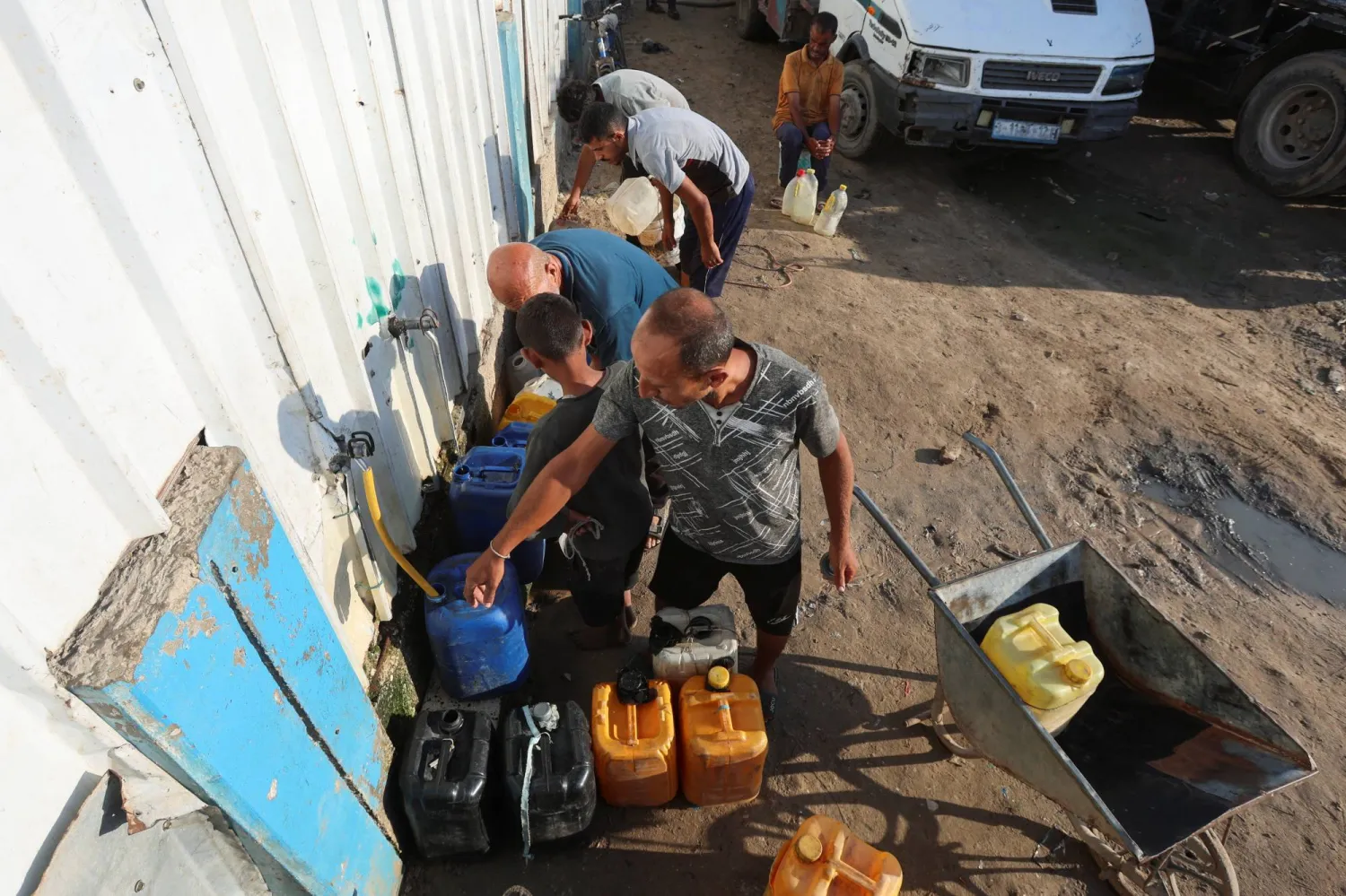 فلسطينيون يملأون أوعية بالماء من مركز توزيع في دير البلح بوسط غزة الثلاثاء (رويترز)