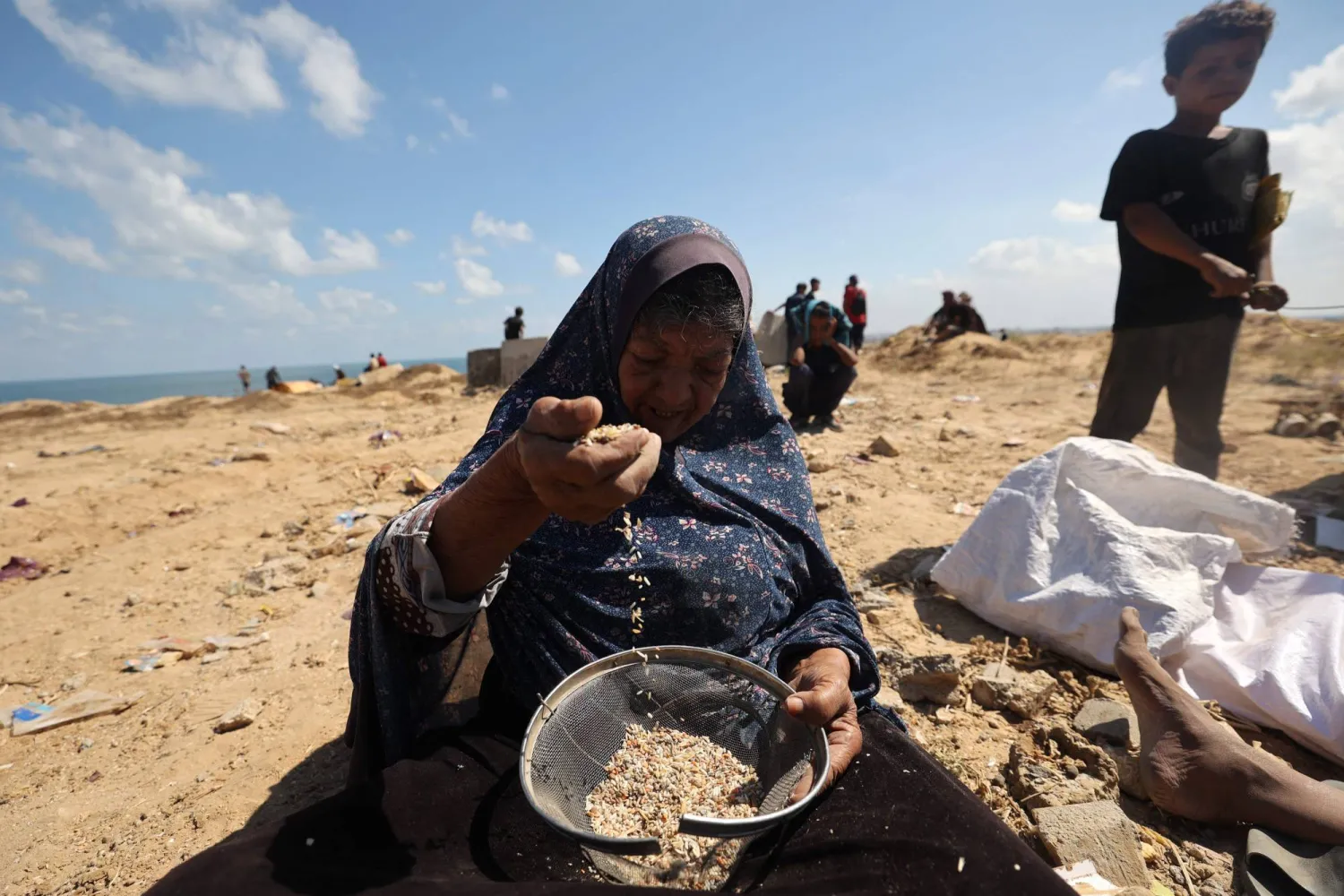 سيدة فلسطينية تبحث عن البقوليات في وسط الرمل في موقع شهد إنزالاً جوياً في مخيم النصيرات في غزة (أ.ف.ب)