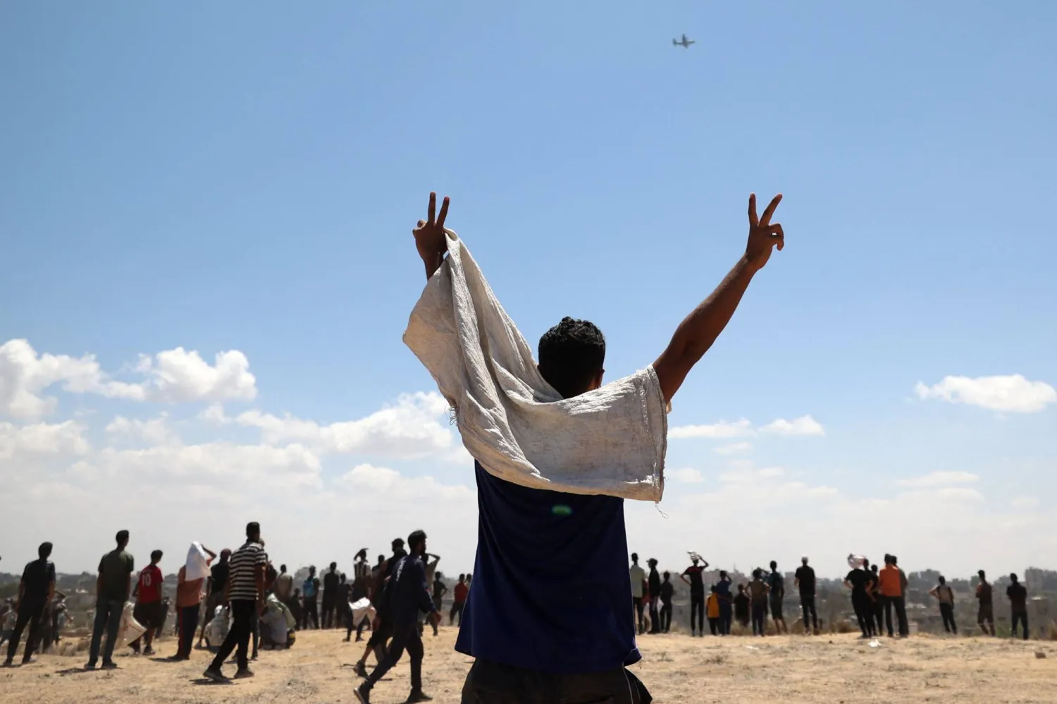 فلسطيني يلوح لطائرة تحمل مساعدات إنسانية فوق النصيرات بوسط قطاع غزة يوم الثلاثاء (أ.ف.ب)