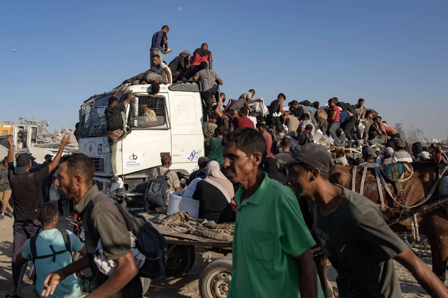 فلسطينيون يتسلقون شاحنات المساعدات للحصول على الغذاء بالقرب من نقطة توزيع مساعدات بجنوب خان يونس في غزة (إ.ب.أ)