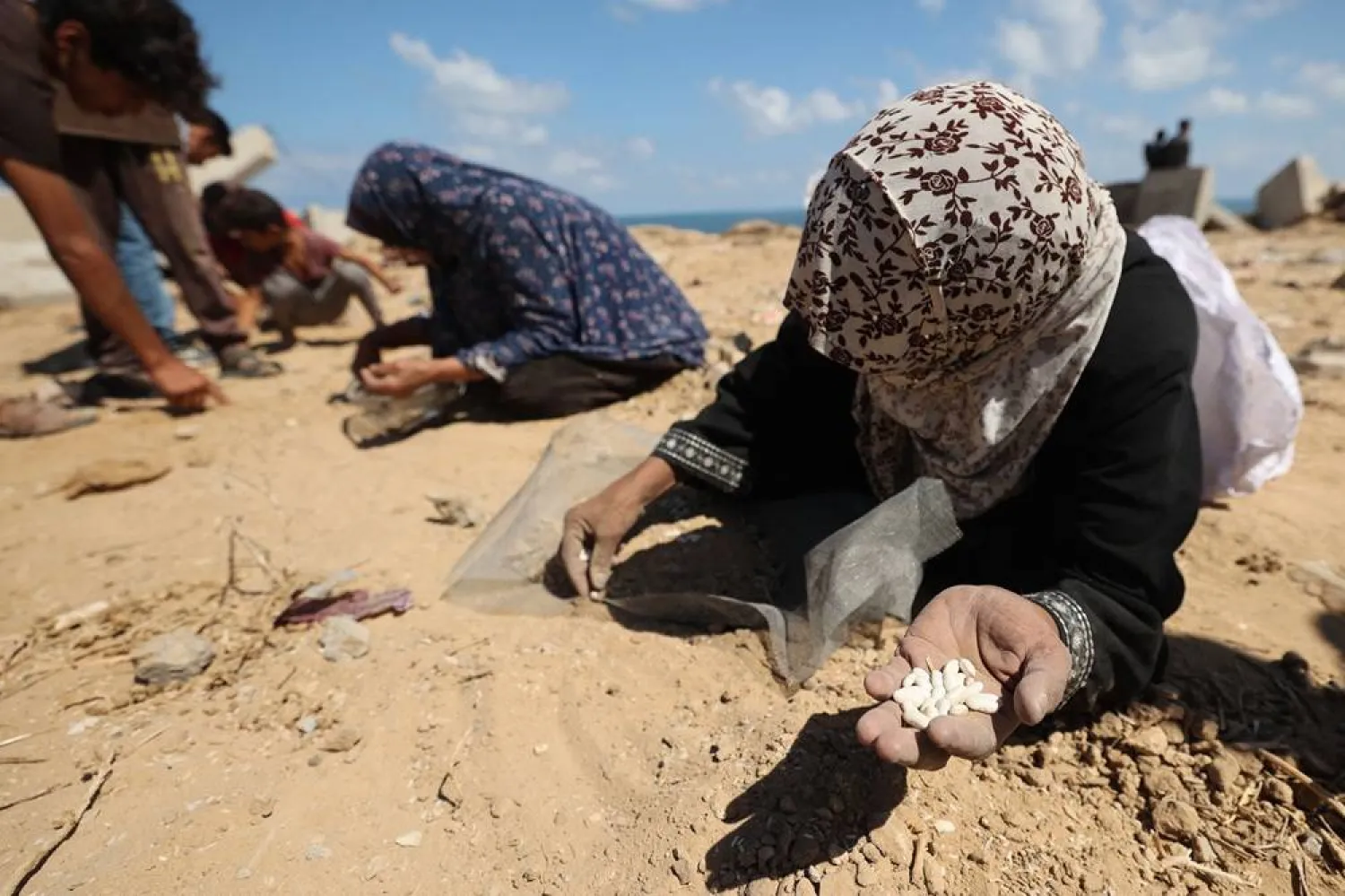 Palestinian women search the sand for legumes or rice in Nuseirat in the central Gaza Strip during an airdrop mission above the Israel-besieged Palestinian territory on August 5, 2025. (AFP)