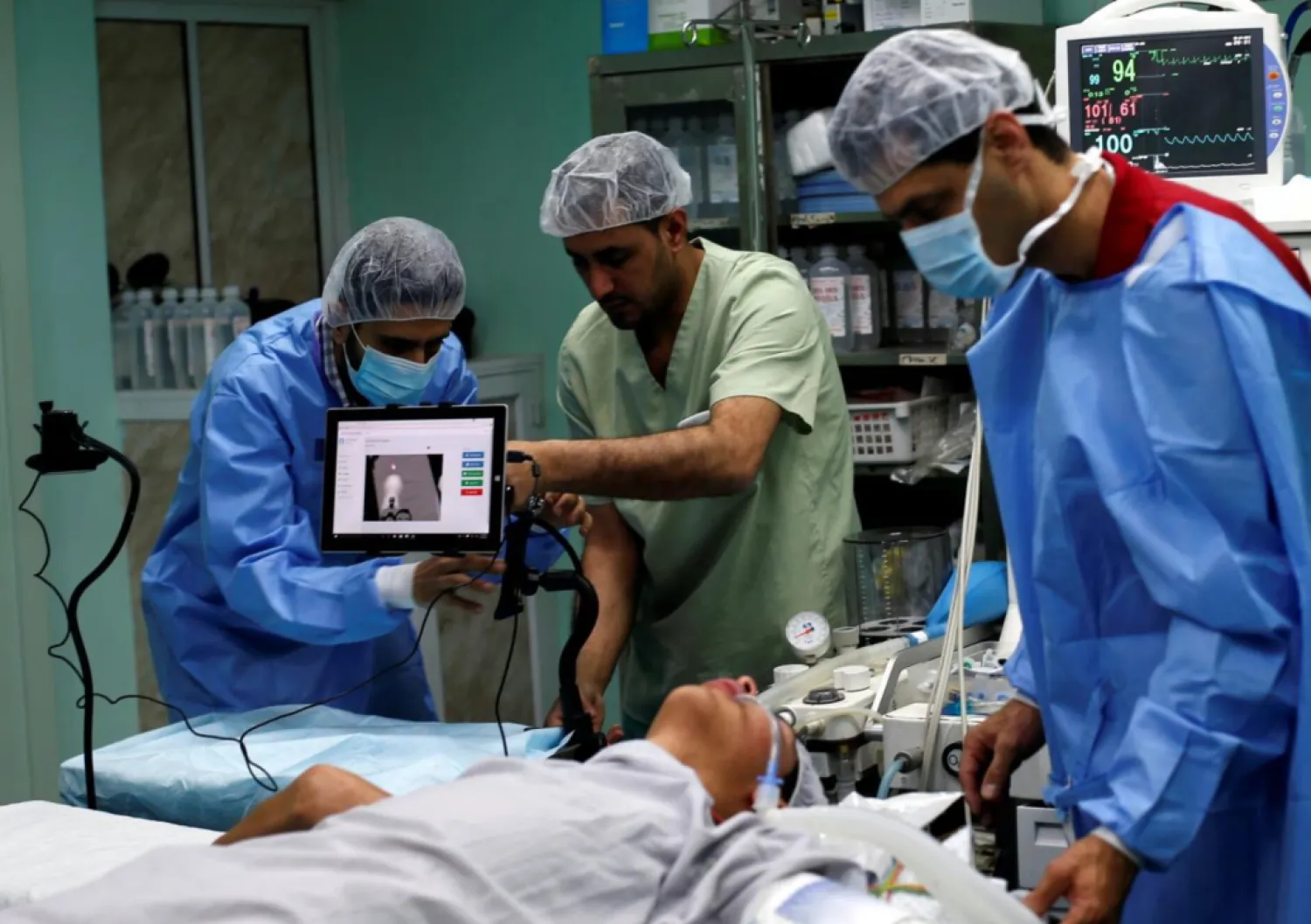 A patient lies on a bed as a technician (L) adjusts a screen before the start of a Proximie surgery, with doctor Ghassan Abu Sitta in Beirut guiding Palestinian surgeon Hafez Abu Khousa in the operating room at Al Awda Hospital in the northern Gaza Strip April 30, 2016. REUTERS/Suhaib Salem
