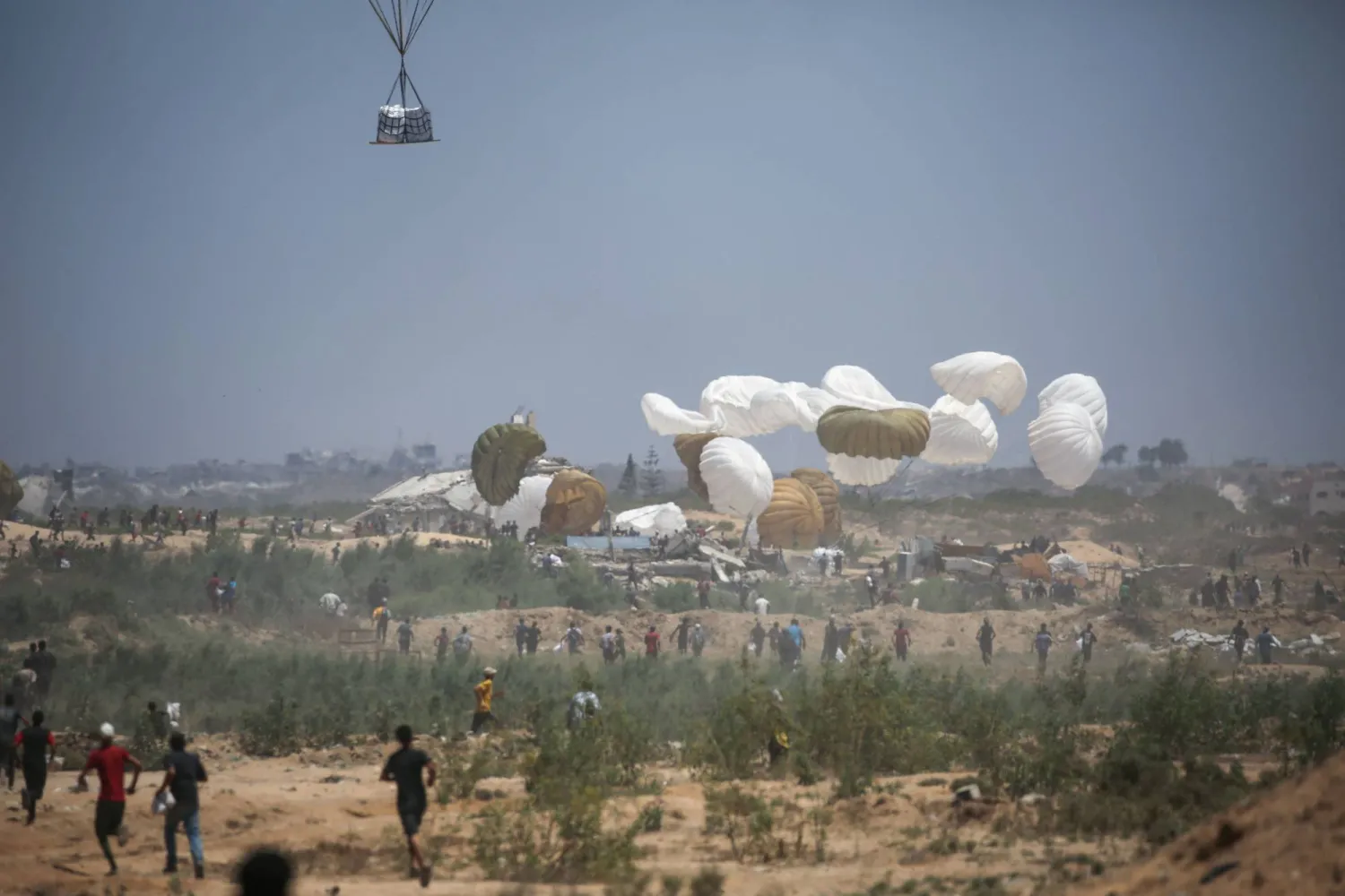 فلسطينيون يركضون إلى موقع هبوط مساعدات بالمظلات في منطقة النصيرات بوسط قطاع غزة 6 أغسطس 2025 (أ.ف.ب)