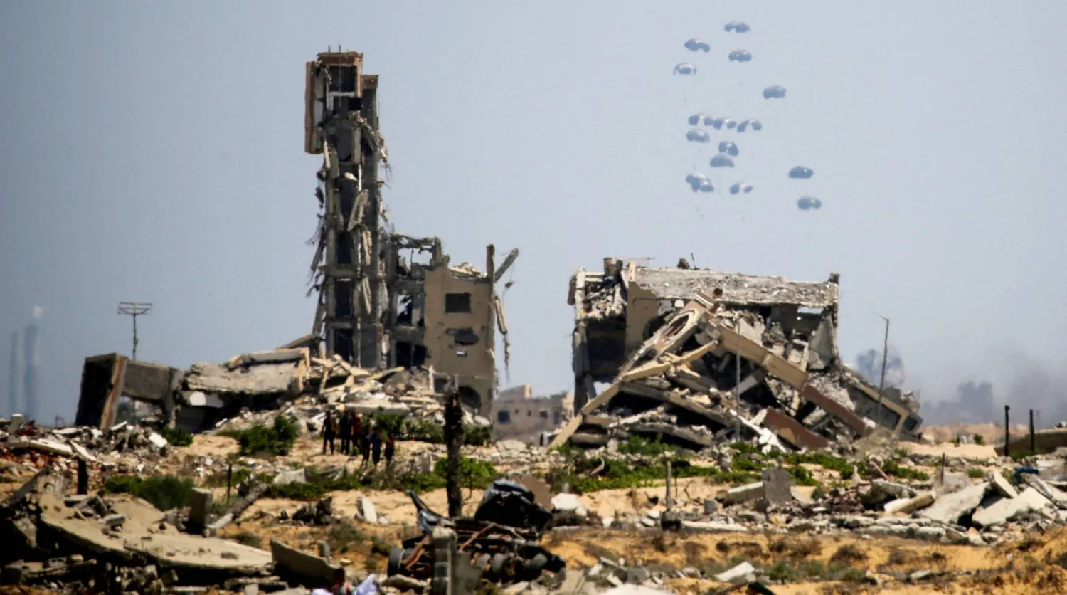  فلسطينيون يشاهدون طرود مساعدات تُلقى من الجو وسط الدمار في منطقة النصيرات وسط غزة أمس (أ.ف.ب)