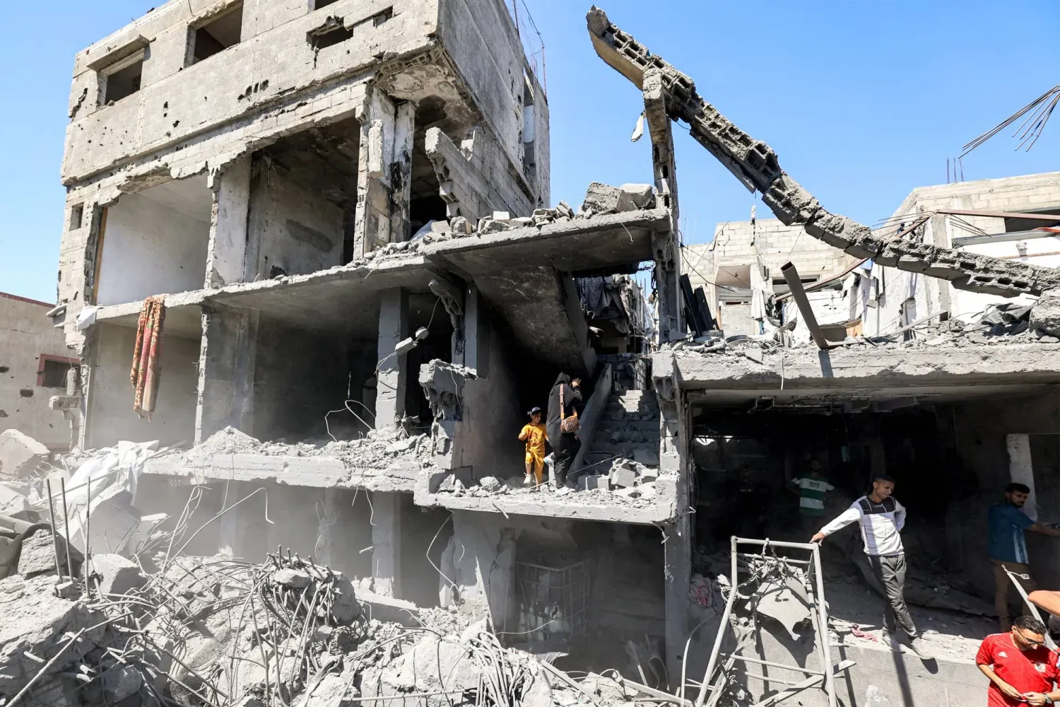 İsrail'in Gazze Şeridi'nin orta kesimindeki el-Bureyc Mülteci Kampı'na düzenlediği hava saldırısı sonucu hasar gören binanın enkazını inceleyen Filistinliler (AFP)