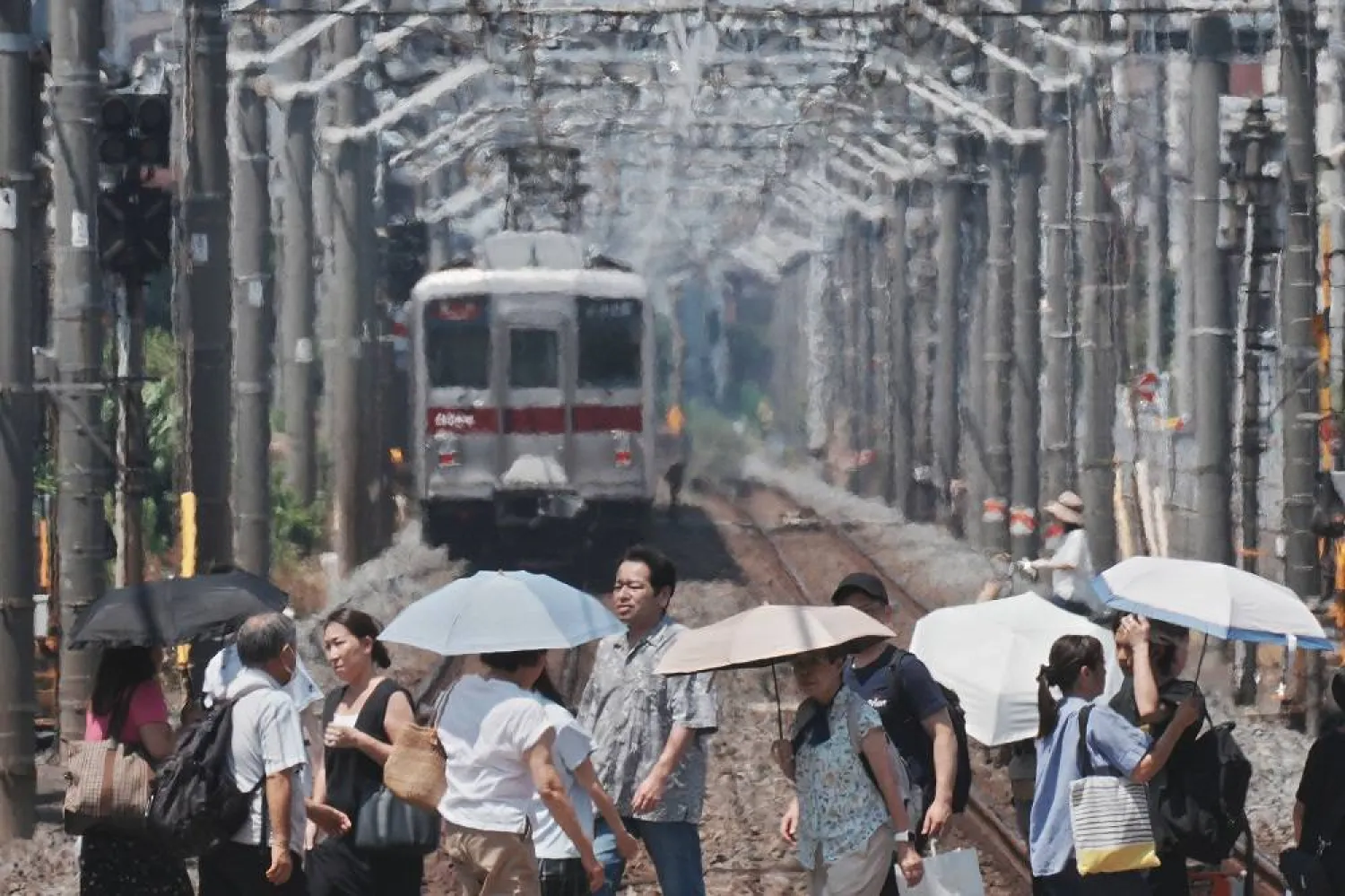 Heat haze is seen in the background while pedestrians with umbrellas cross a railroad on a hot day in Tokyo on August 5, 2025. (AFP)