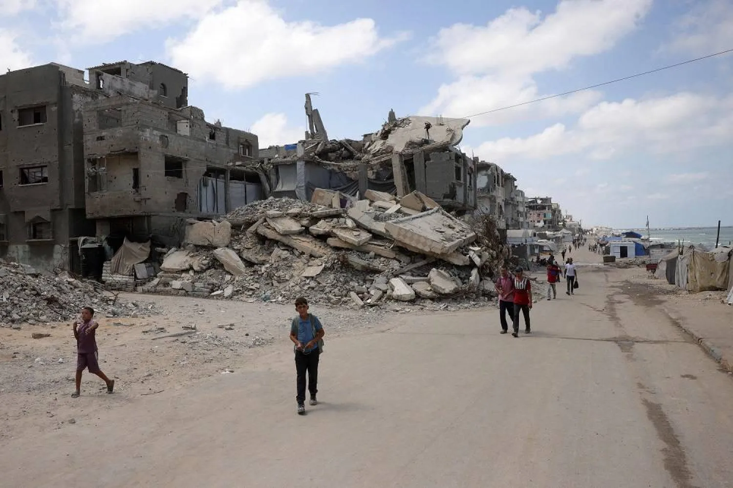 Palestinians walk along a street near war-damaged buildings along the shore in Gaza City on August 8, 2025. (AFP)