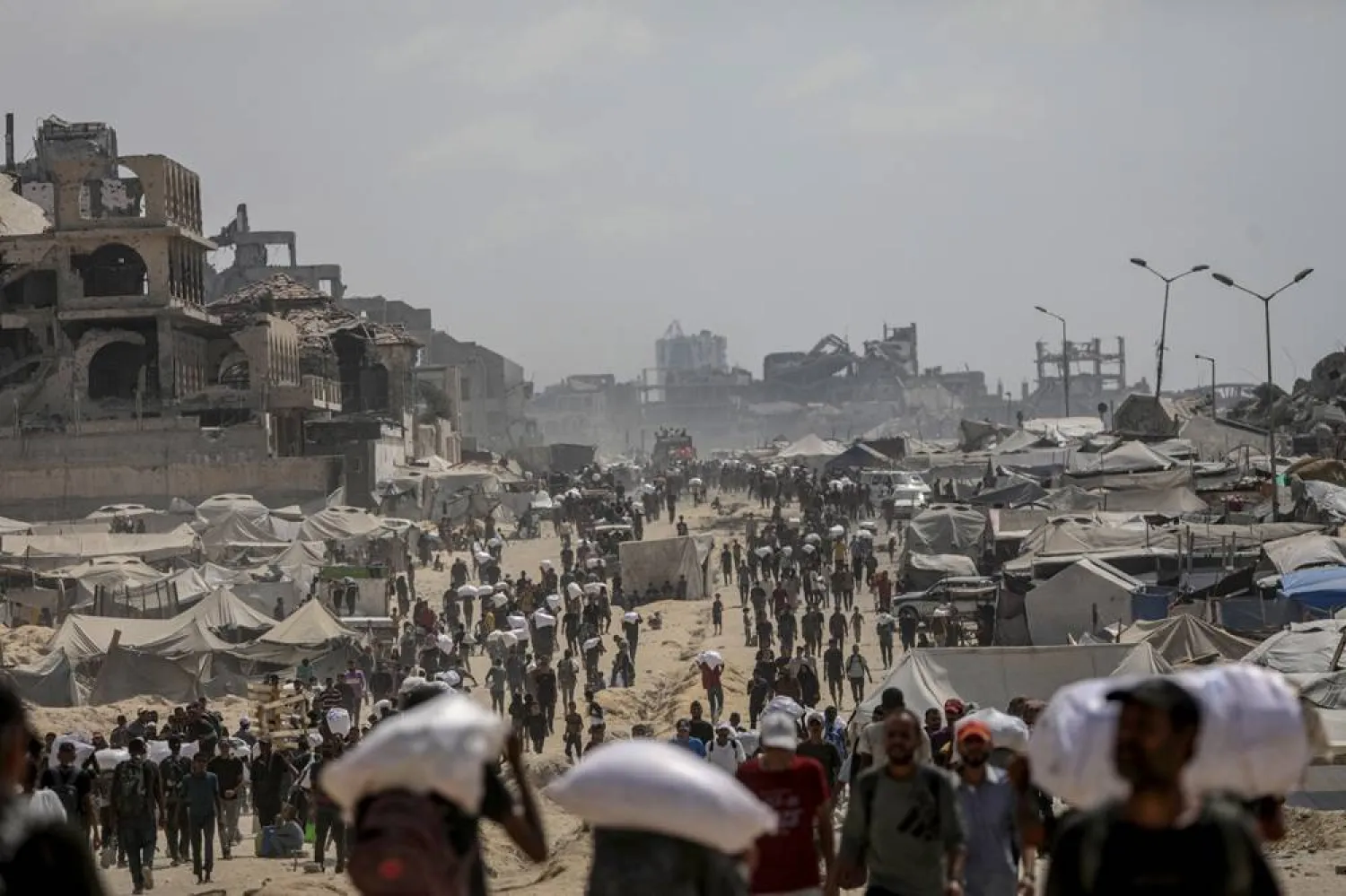 Internally displaced Palestinians carry bags of flour near a food distribution point in Zikim, northern Gaza Strip, 08 August 2025. (EPA)