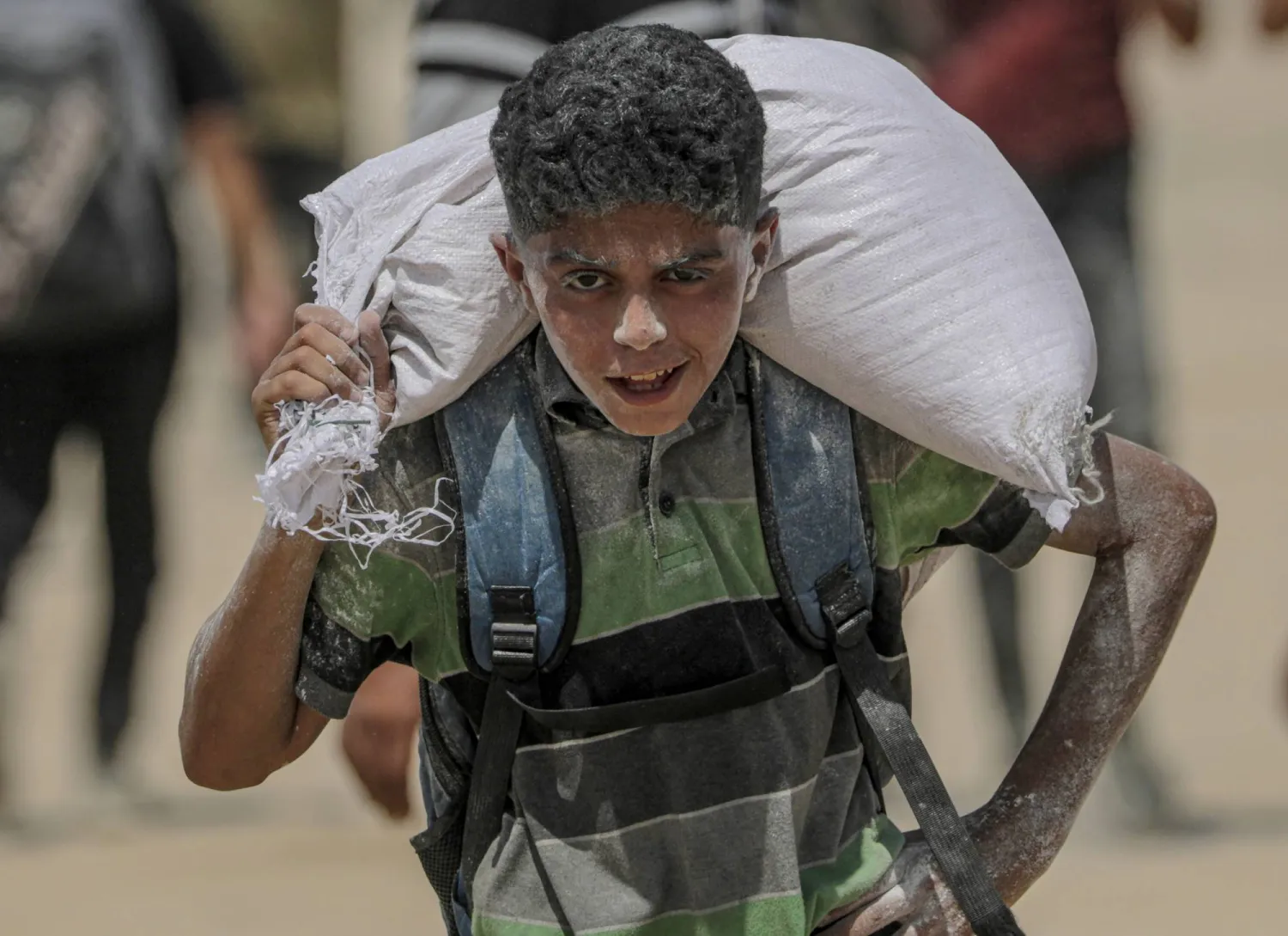 شاب فلسطيني يحمل جوال دقيق قرب نقطة توزيع أغذية في زيكيم شمال قطاع غزة (إ.ب.أ)