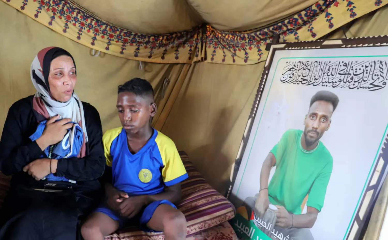 Doaa, the widow of late soccer player Suleiman Al-Obeid, known as the "Palestinian Pele," who was killed by an Israeli strike targeting people waiting for humanitarian aid, according to the Palestine Football Association, looks at his picture while holding his shorts, as her son sits beside her inside their tent in Gaza City August 9, 2025. REUTERS/Ebrahim Hajjaj 