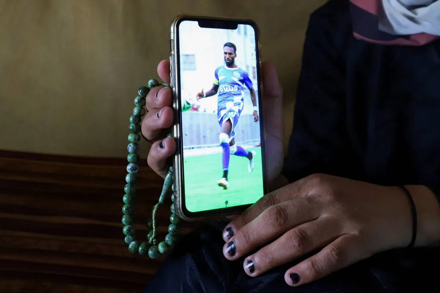 Filistinli futbolcu Süleyman el-Ubeyd'in eşi, Gazze Şeridi'ndeki bir çadırın içinde cep telefonunda onun fotoğrafını gösterirken (Reuters)
