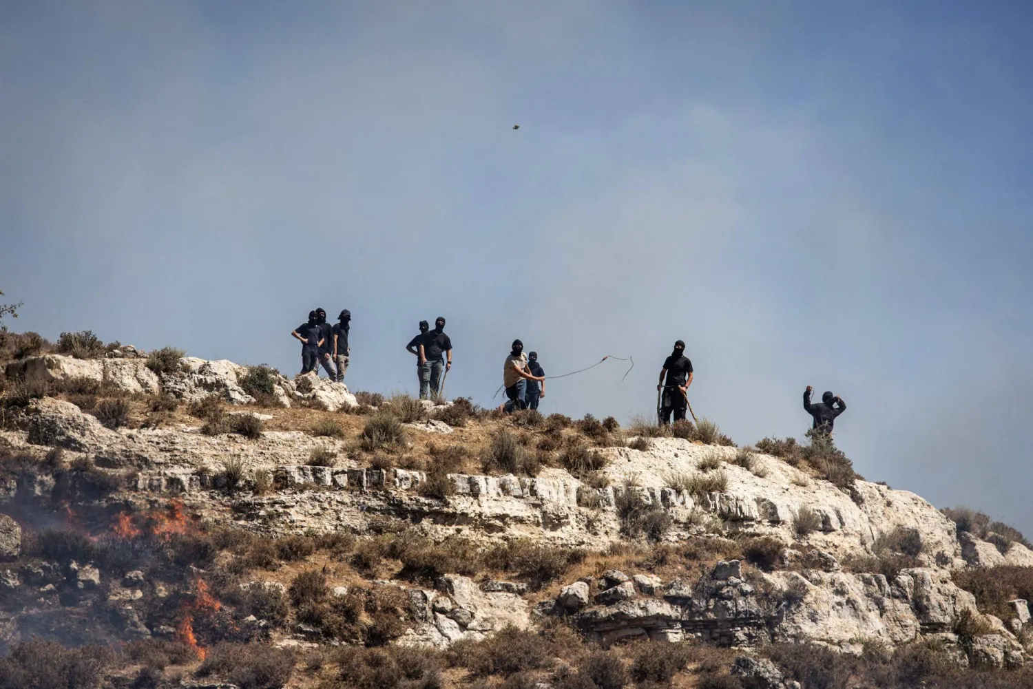 مستوطنون إسرائيليون ملثّمون يرشقون الفلسطينيين بالحجارة في بلدة سنجل بالضفة الغربية (أ.ف.ب)