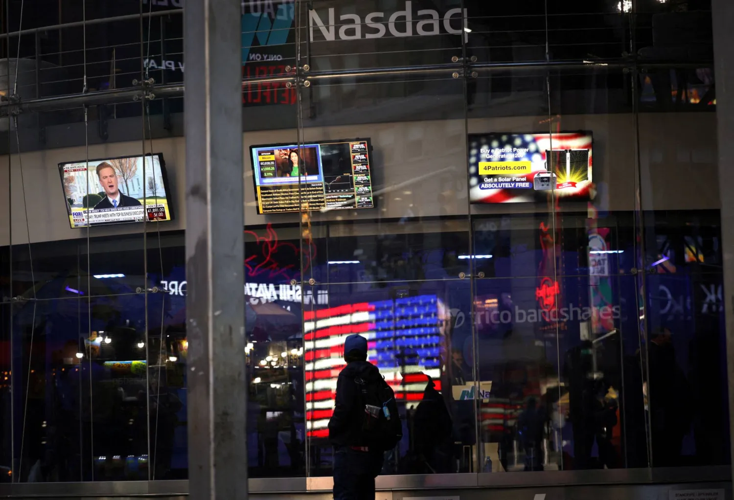 أشخاص يمشون أمام موقع بورصة «ناسداك» مع افتتاح أسواق الأسهم الأميركية (رويترز)