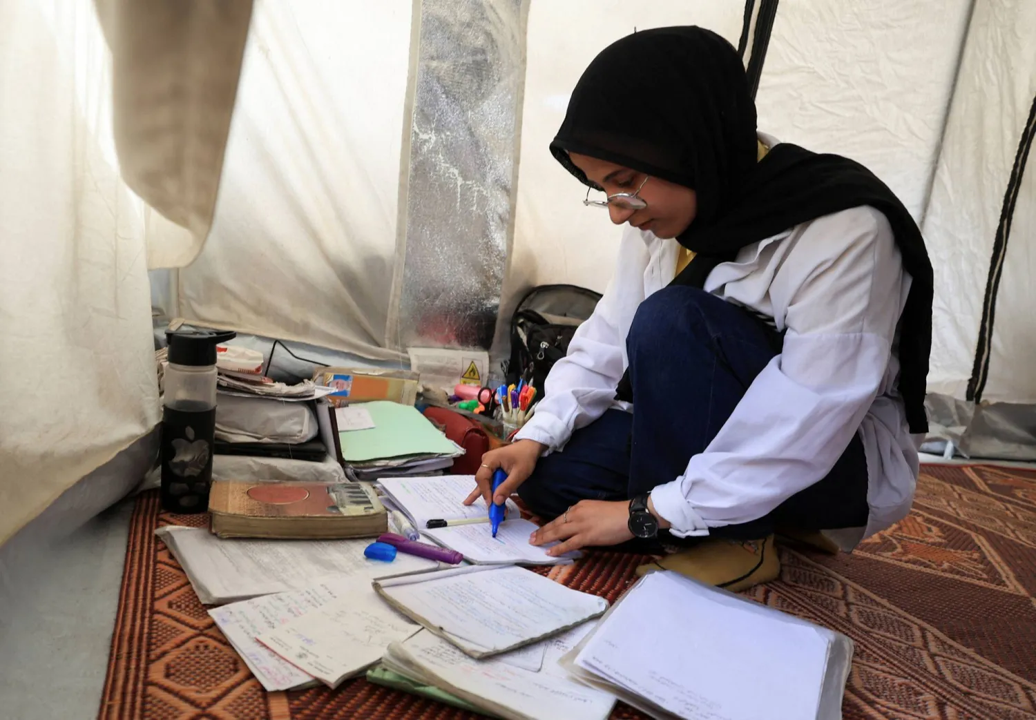 تجلس الطالبة الفلسطينية النازحة ياسمين الزعانين البالغة من العمر 19 عاماً داخل خيمة تفرز دفاترها وكتبها في ملجأ مدرسي بمدينة غزة (رويترز)