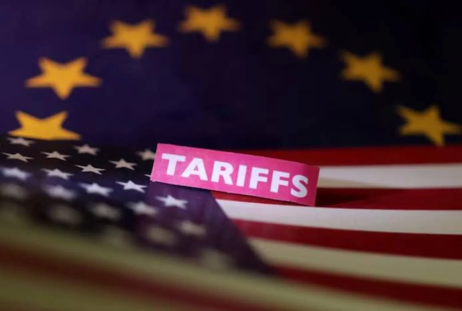 علما الولايات المتحدة والاتحاد الأوروبي وشارة تحمل عبارة «رسوم جمركية» في صورة توضيحية (رويترز)