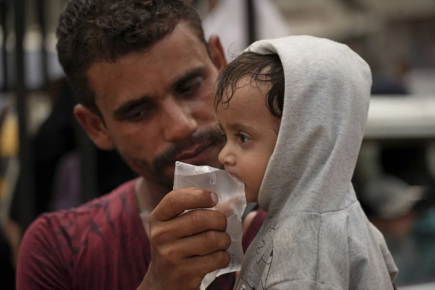 فلسطيني يعطي طفلاً شربة ماء من كيس اشتراه بشيقل في أجواء بالغة الحرارة بمدينة غزة يوم الثلاثاء (أ.ب)