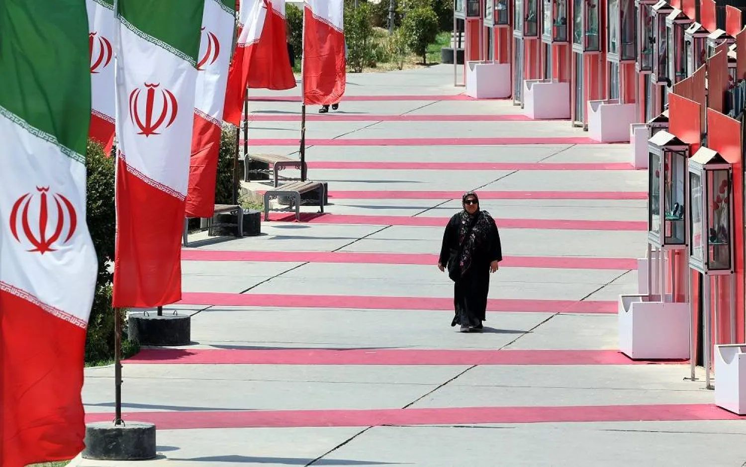 A woman walks next to Iranian national flags in a street in Tehran, Iran, 10 August 2025. (EPA)