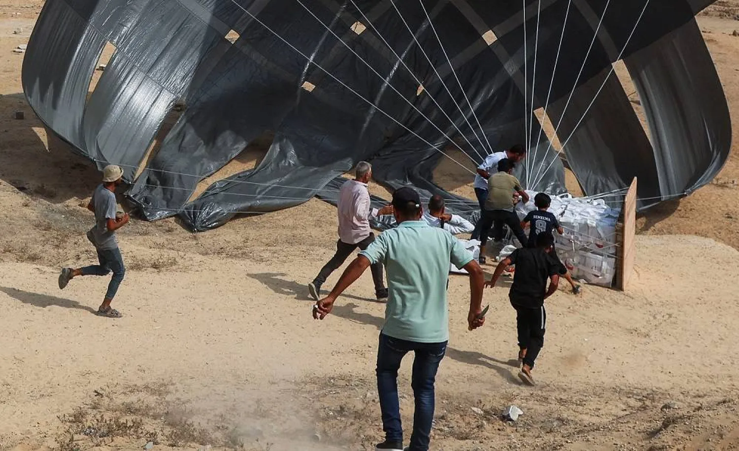 Palestinians run to collect food items as aid packages are dropped from an airplane, in Deir Al-Balah, in the central Gaza Strip August 12, 2025. (Reuters)