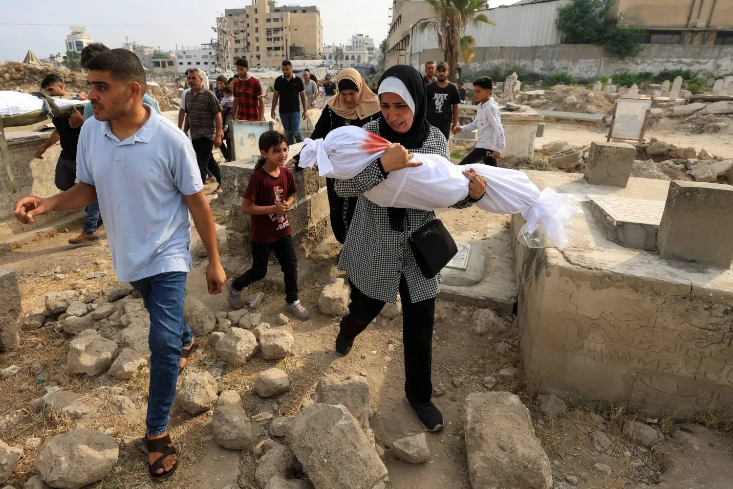 Filistinli Süha Tafeş, sabahın erken saatlerinde evlerine düzenlenen İsrail saldırısında hayatını kaybeden torunu Sare Ebu Def'in cenazesini taşıyor. (Reuters)