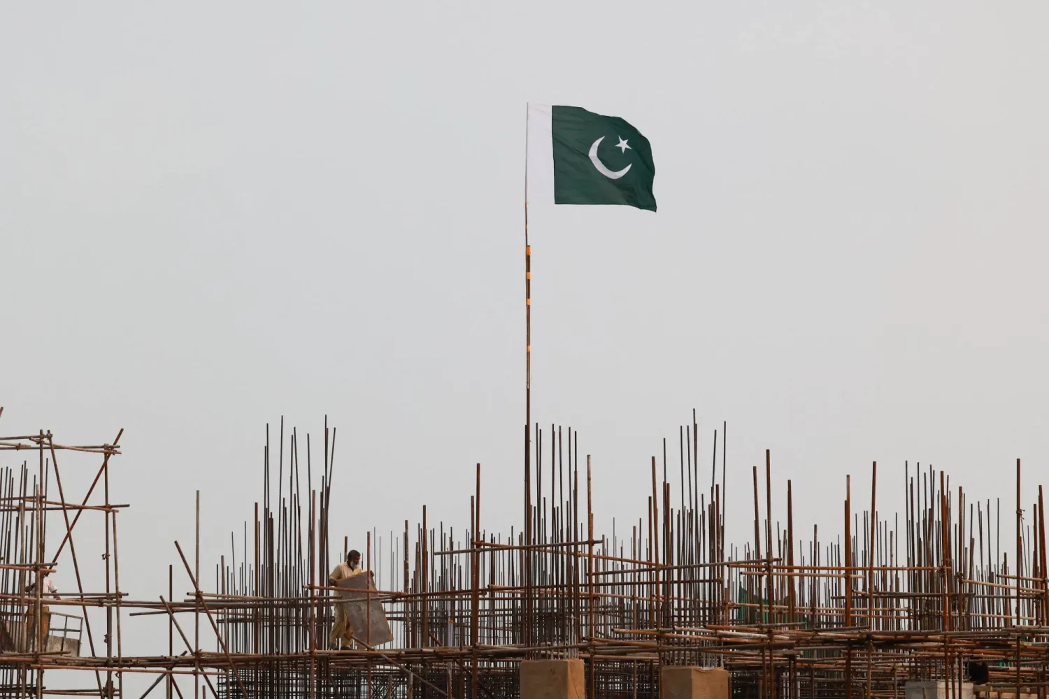 A Pakistani flag flutters over iron scaffoldings as a laborer works at a construction site on the eve of Pakistan's Independence Day celebrations, in Lahore, Pakistan August 13, 2025. REUTERS/Akhtar Soomro