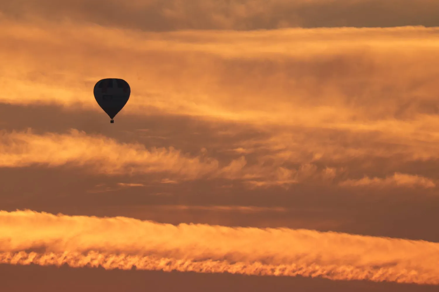 10 August 2025, Baden-Wuerttemberg, Uttenweiler: A balloon drifts in the orange-colored morning sky shortly before sunrise. Photo: Thomas Warnack/dpa