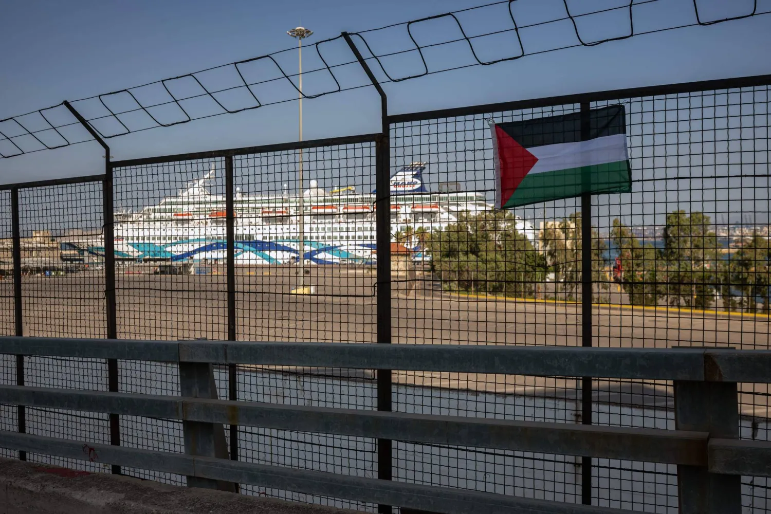 This photo shows a Palestinian flag hung by demonstrators on a fence of the Port of Piraeus during a protest against the arrival of the 'Crown Iris' (in the background) a cruise liner carrying Israeli tourists in Athens, on August 14, 2025. (Photo by Angelos TZORTZINIS / AFP)