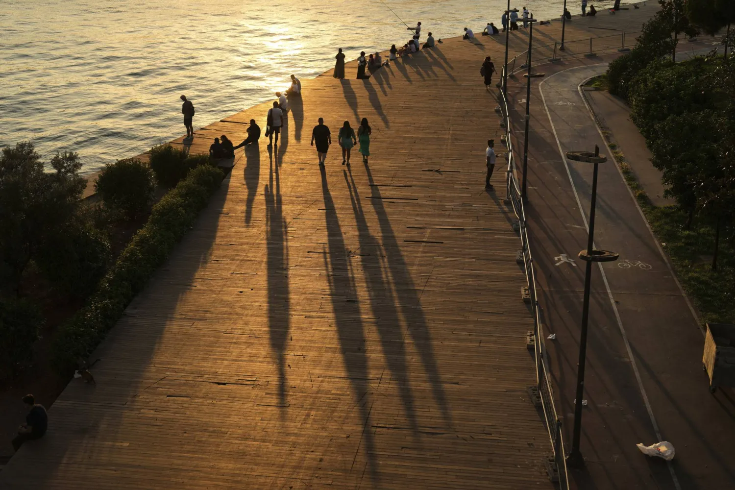 People cast long shadows on the ground as they gather in a promenade next to the Bosphorus during a hot summer day in Istanbul, Türkiye, Tuesday, Aug. 12, 2025. (AP Photo/Francisco Seco)