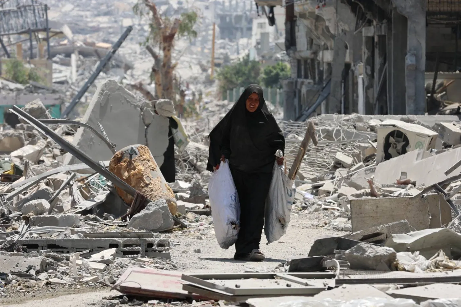 امرأة فلسطينية وسط الأنقاض تحمل أخشاباً في أكياس بحي التفاح في مدينة غزة (أ.ف.ب)