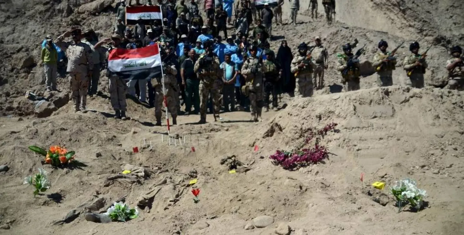 Iraqi soldiers salute as they stand next to a mass grave for soldiers from Camp Speicher who have been killed by ISIS militants. REUTERS/Stringer