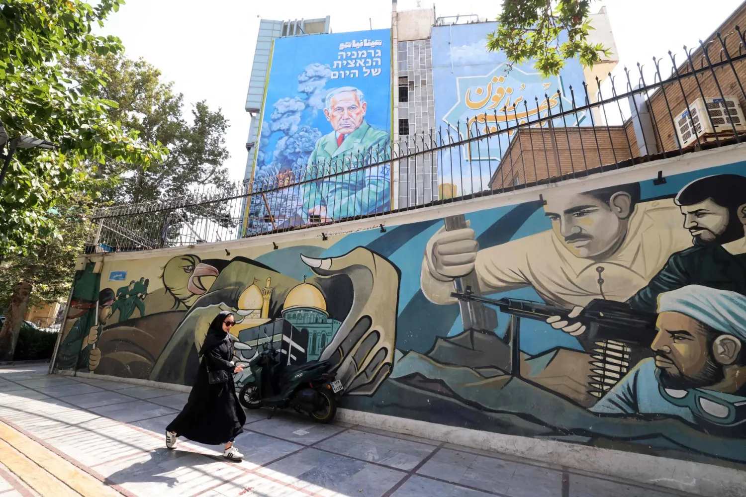 An Iranian woman walks on a sidewalk next to a recently unveiled billboard bearing the portrait of Israel's Prime Minister Benjamin Netanyahu with text in Persian reading "Hitanyahu" and text in Hebrew reading "Germany's Nazi of today" at Palestine Square in central Tehran on August 11, 2025. (Photo by ATTA KENARE / AFP)