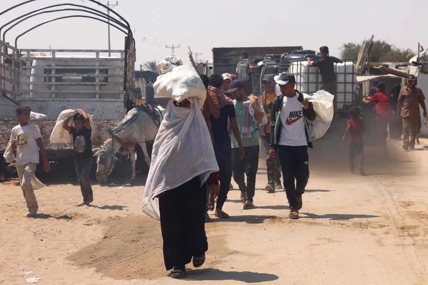 A Palestinian woman carries humanitarian aid, she gathered after an aid drop, as she walk in the Mawasi area of Rafah in the southern Gaza Strip on August 18, 2025. (AFP)