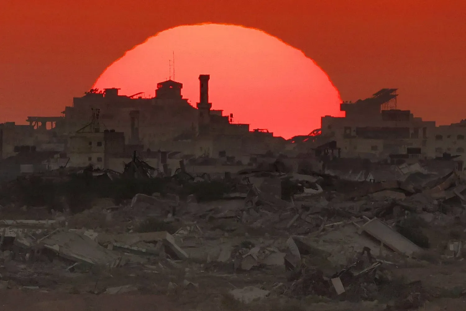 Dün çekilen ve Gazze Şeridi'nin yıkık binalarının ardında güneşin batışını gösteren bir fotoğraf (AFP)