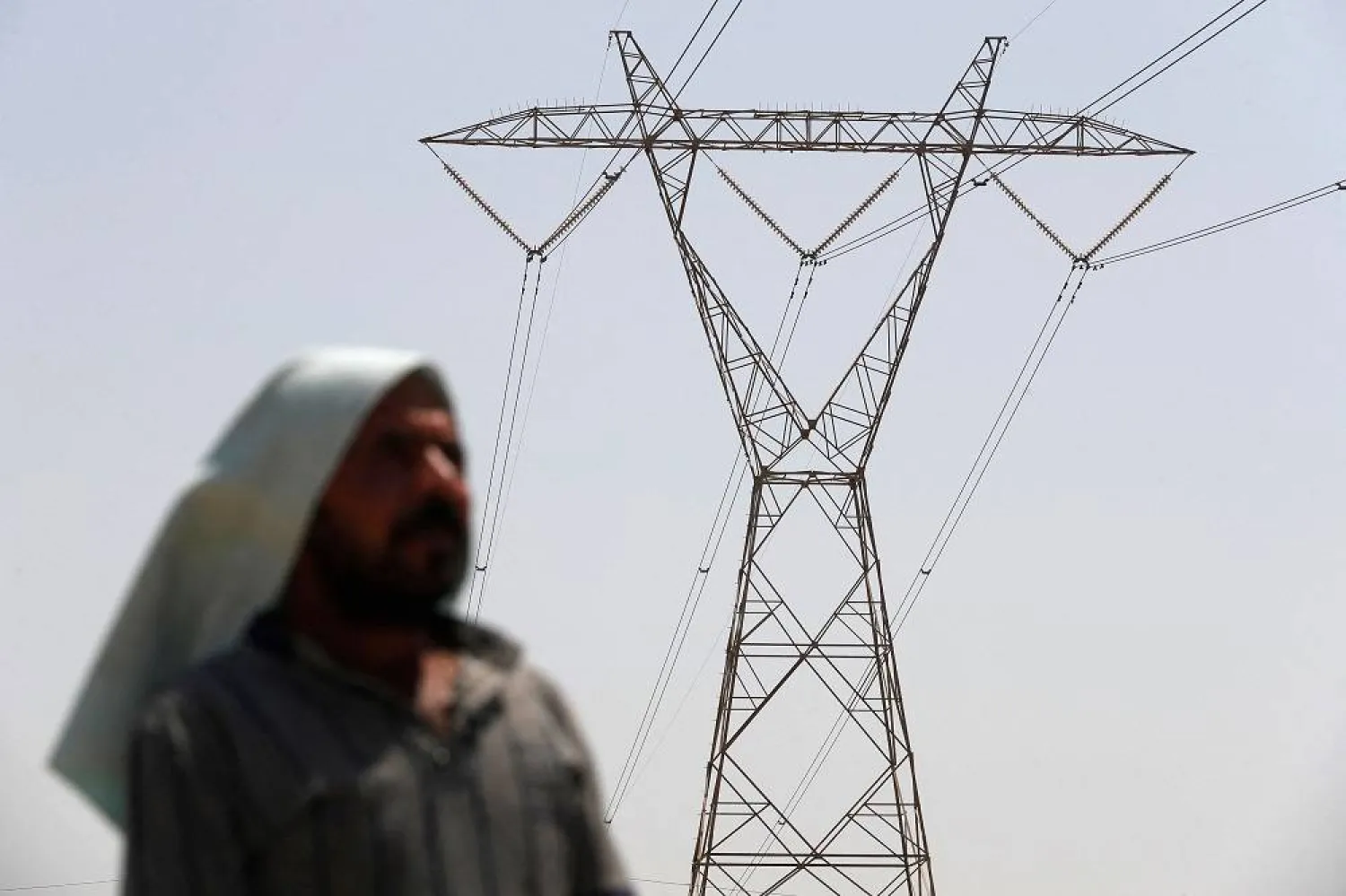 An Iraqi man stands under an electricity transmission tower south of Hilla city on August 10, 2025, amidst rising temperatures, chronic water shortages and power cuts. (AFP)
